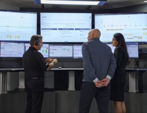 3 people in suites conversing with monitors in the background