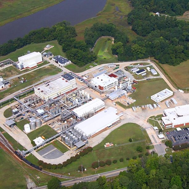 The image is an aerial view of a large building surrounded by grass and trees in a suburban area.