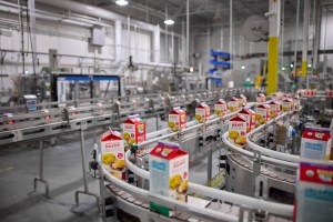 A long shot of an automated production line in a factory. Cardboard cartons of half and half dairy product are moving along a series of curved and straight conveyor belts.| Platinum Equity