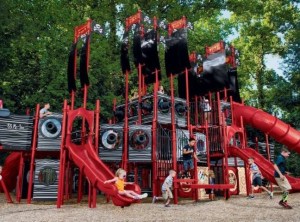 Group of children climbing and playing on a large multilevel playground structure with slides, nets, and towers. | Platinum Equity