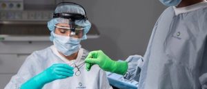 Two medical staff in full protective gear handle surgical instruments in a clinical setting, wearing masks, gowns, and bright green gloves. | Platinum Equity