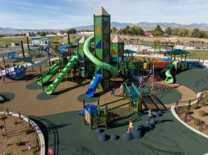 Large outdoor playground with tall climbing towers, twisting green slides, rope structures, and children playing across the activity areas. | Platinum Equity