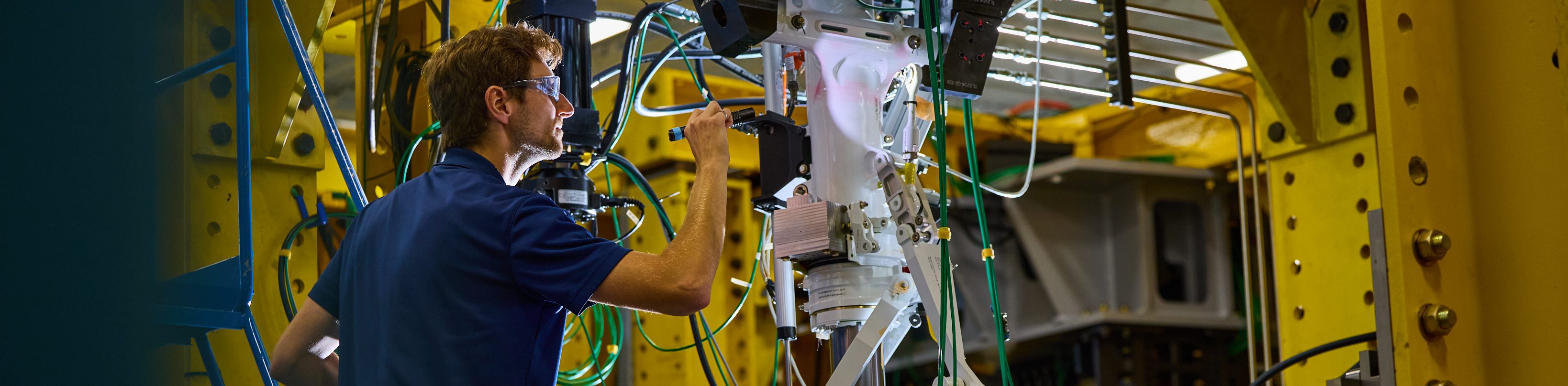 Technician wearing safety glasses inspecting automated industrial equipment inside a factory | Platinum Equity