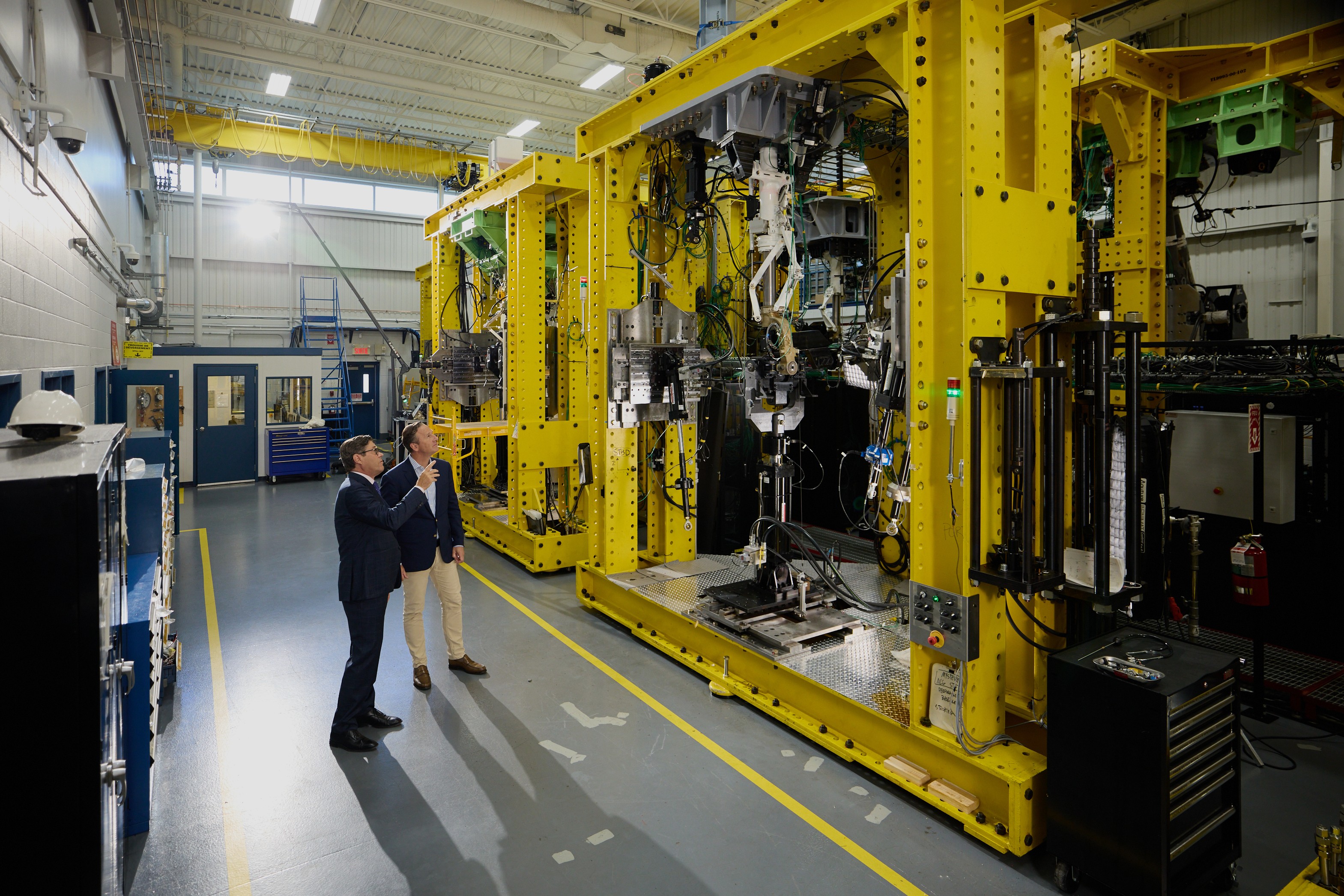 Two people in business attire and safety glasses walking through a factory beside large industrial machinery | Platinum Equity